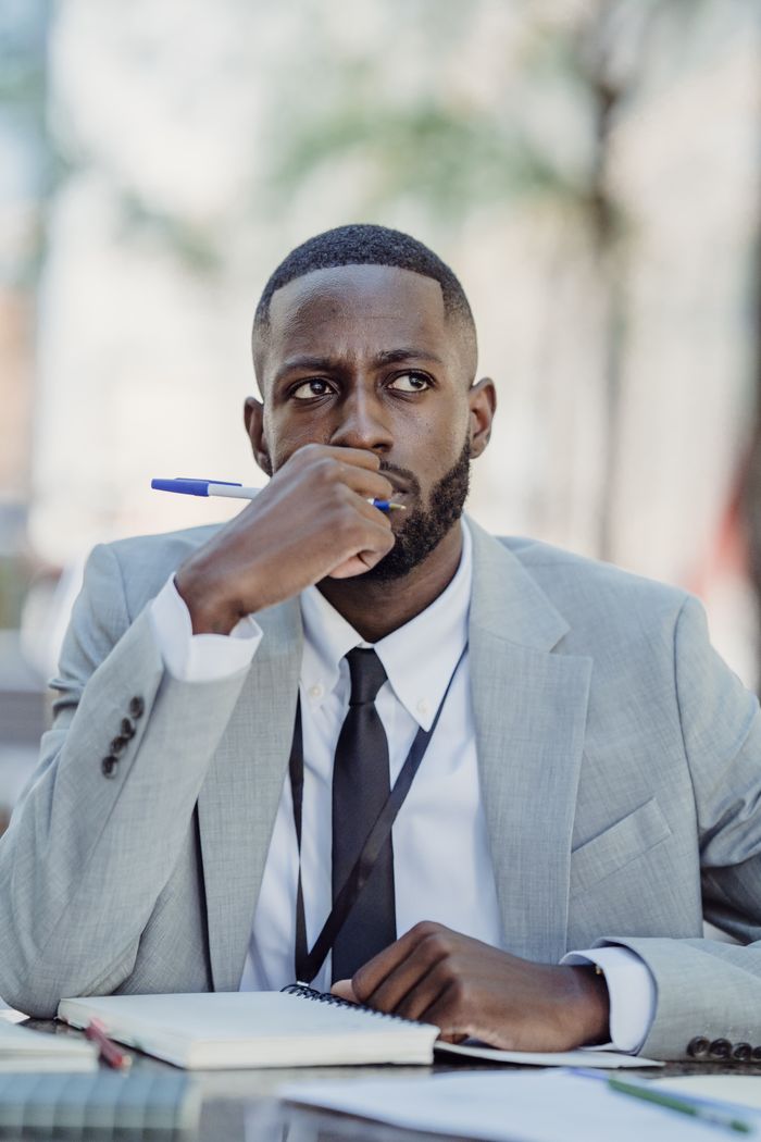 Crafting Captivating Headlines: Your awesome post title goes here A businessman in a grey suit sits outdoors pondering with a pen and notebook.